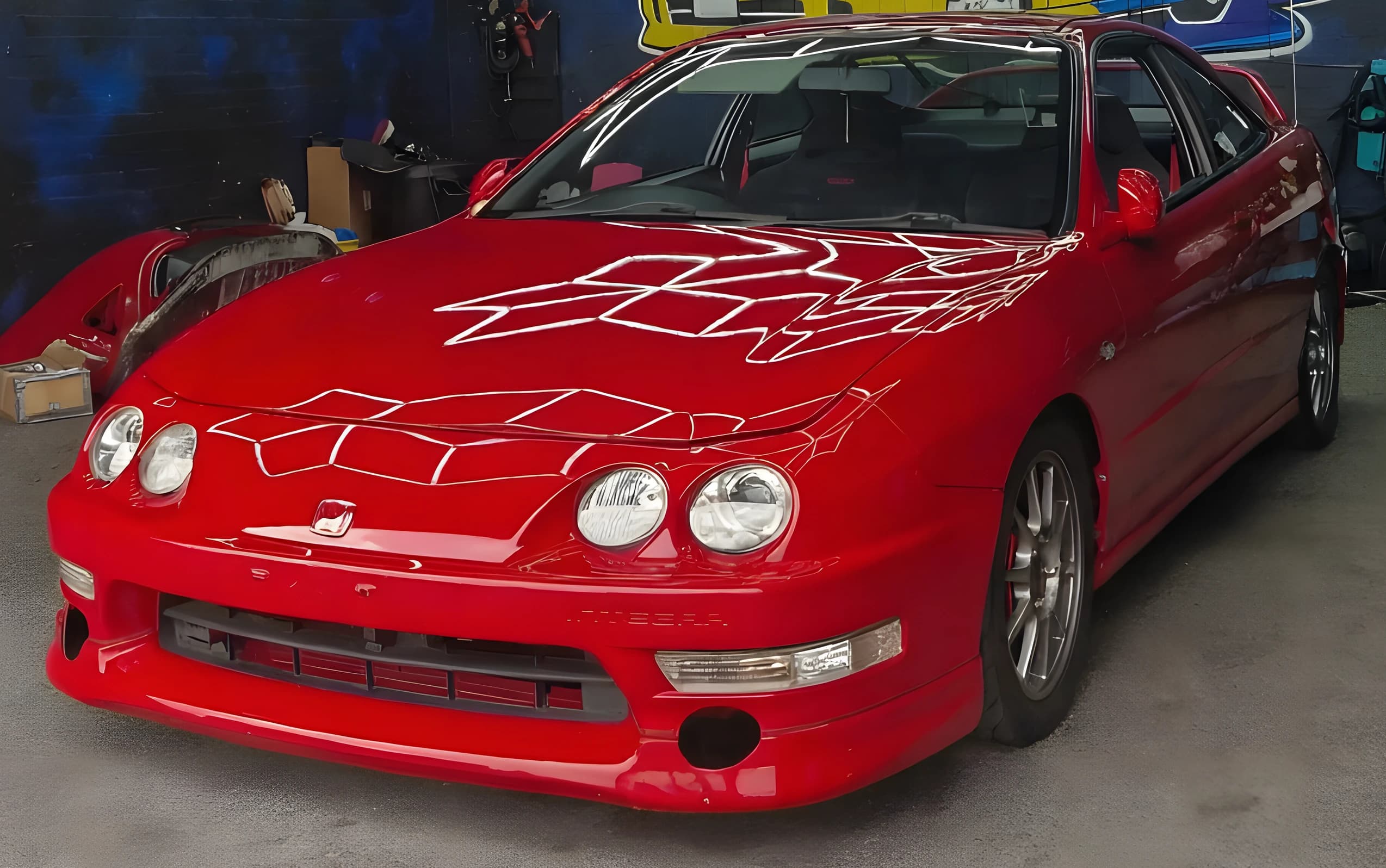 A red coupe in front of the studio mural